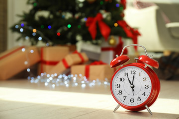 Red alarm clock near Christmas tree in room. Celebration time