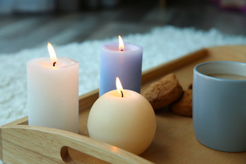 Burning candles and cup of coffee on wooden tray