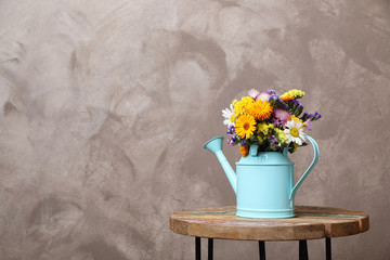 Watering can with beautiful wild flowers on table against grey background