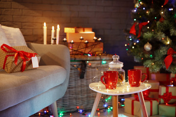 Cups and jar with cookies on table in room decorated for Christmas. Stylish interior