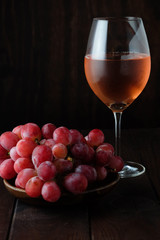 Glass of pink wine and red grapes on dark background