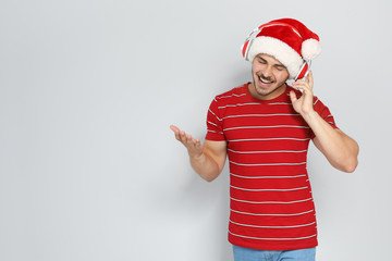 Fototapeta na wymiar Young man in Santa hat listening to Christmas music on color background