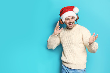 Fototapeta na wymiar Young man in Santa hat listening to Christmas music on color background