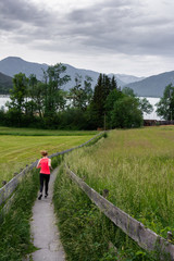 Fototapeta na wymiar Young woman running along fenced path through field