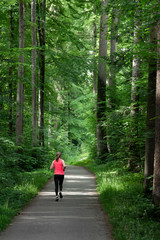 Young woman running along path through green forest.