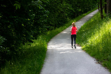 Obraz premium Young woman running along curved path through green forest.