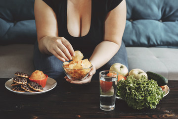 Food addiction, dieting concept. Young overweight woman fighting the temptation to eat chips,...
