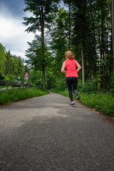 Young woman running along curved path through green forest.