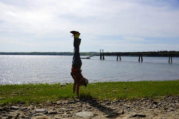 Man Handstands on rocky grassy beach with Pier