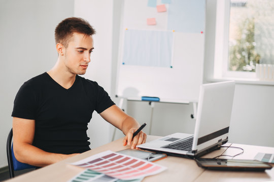 Young male designer using graphics tablet at work. Man drawing working with color samples at studio