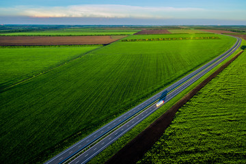 White trucks driving on asphalt road along the green fields in rural landscape. Road seen from the...