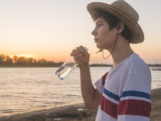 young boy with bottle of water standing on the beach on a sunset