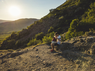 portrait of man sitting on the mountain with backpack in casual clothes during beautiful sunset
