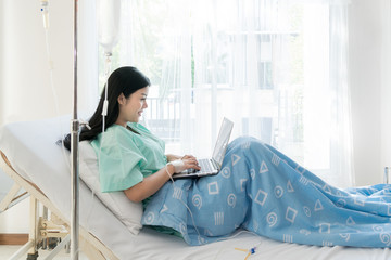 Asian woman sick patient lying in a hospital bed using a laptop for relax when she recovering for...