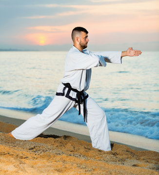 Man in uniform doing taekwondo exercises at  sunset sea shore