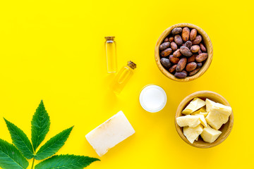 Cosmetics with cocoa butter for skin care. Cocoa beans and cocoa butter in bowl, soap, cream, oil or lotion in small bottles on yellow background top view copy space