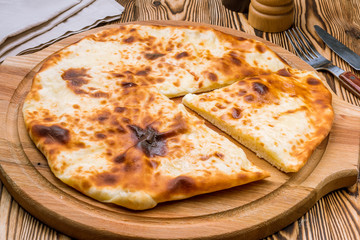 Ossetian pie with cheese on wooden background