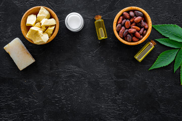 Beautiful composition with cocoa butter cosmetics. Cocoa butter and cocoa beans near homemade soap, moisturising cream, oil or lotion in small bottles on black background top view space for text