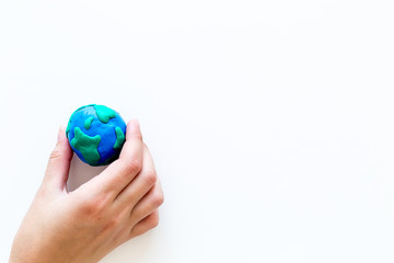 Earth. Hand hold plastiline symbol of planet Earth globe on white background top view copy space