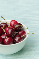 A bowl of red cherries on a teal tablecloth