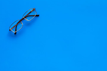 One glasses with transparent lenses on blue background top view copy space