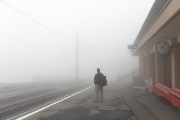 A man waiting for a train to arrive on a foggy day