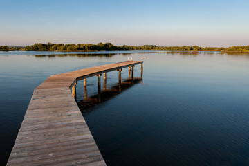 Fototapeta premium Dock jutting out into the water with Roseate spoonbill taking off from end