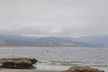Kayak in ocean, faraway. Coast on background. Foggy.