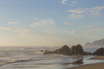 Fototapeta na wymiar Oregon coast. Rock formation in water with coastal line in background. Hazy air. Low sun.
