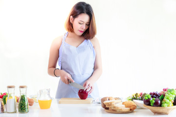 Health concept: A beautiful pregnant asian girl is cutting the apple by using a knife for cooking salad in the kitchen at her house. Charming girl is a good housewife with isolated on white background