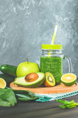 healthy green smoothie with ingredients on a wooden table: apple, kiwi, lime, spinach, mint, avocado, cucumber