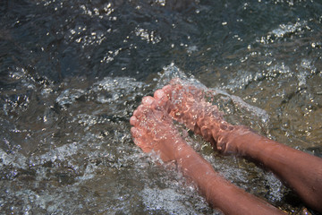 A young black child dangling his feet in a river or lake