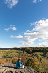 A woman sitting on a rock overlook in the fall