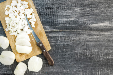 Sliced onions on a board with an aged knife on a dark wood background with copy space. Image of onion cutting.