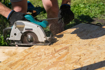 a man sawing a Board with a power tool, chips fly in all directions. Construction, wood processing