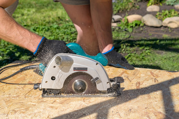 a man sawing a Board with a power tool, chips fly in all directions. Construction, wood processing