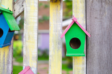Little bird house hanging on wooden fence.