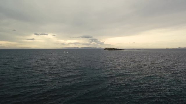 Flying over the sea on a cloudy day. Small island on the horizon.