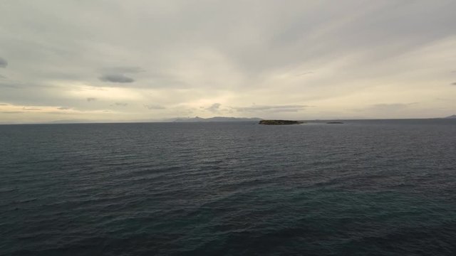 Flying over the sea on a cloudy day. Small island on the horizon.