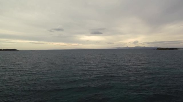Flying over the sea on a cloudy day. Small island on the horizon.
