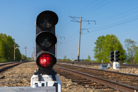 Traffic lights on ground level at the railway. Red light is turned on. Railroad on a sunny day at the background.