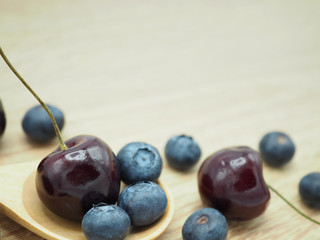 Fresh cherry and blueberry with spoon on wooden background. Healthy food and diet.