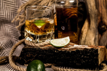 bottle of rum whiskey bourbon and a glass with ice on a wooden background