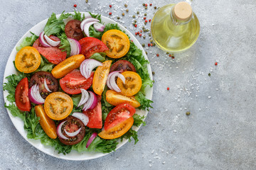 Delicious summer salad of colorful (yellow, red and black) ripe tomatoes, red onions and lettuce with spices. Healthy dinner or lunch