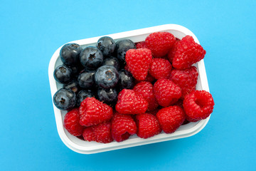 Independence day, happy fourth of july and sweet dessert concept with close up on the american flag made of raspberries and blueberries, isolated on minimalist blue background