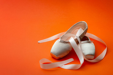 Ballet dancing concept with a pair of silk shoes isolated on minimalist bright orange background © Victor Moussa