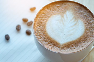 Latte art coffee and roasted coffee beans with papernote at morning time with sunlight on wooden table background.