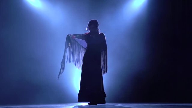 Flamenco. Woman is dancing with a manton in the hands of a Spanish incendiary dance. Llight from behind. Smoke background. Silhouette. Slow motion