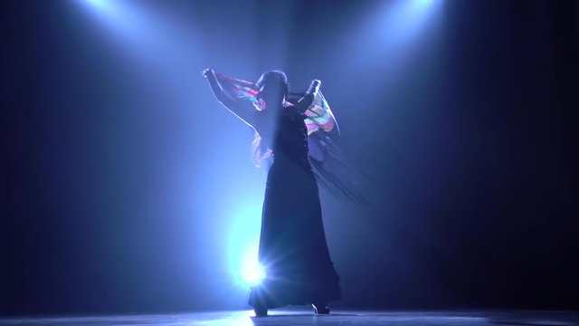 Dancing woman is with a manton in the hands of a Spanish incendiary dance. Llight from behind. Smoke background. Silhouette. Slow motion