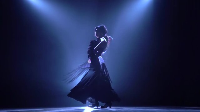 Flamenco. Woman is dancing with a manton in the hands of a Spanish incendiary dance. Llight from behind. Smoke background. Silhouette. Slow motion